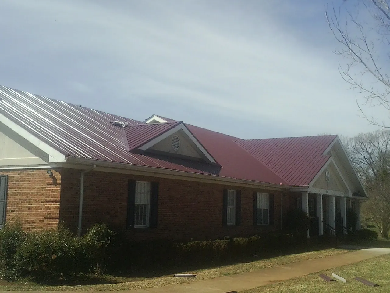 Red metal roof with gabled entries on a long brick building, from a Hail Damage Roof Repair job in Ocean Isle Beach