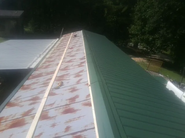Old rusted panels beside newly installed green metal roofing — Wind Damage Roof Repair by Roofing Brothers in Ocean Isle Beach