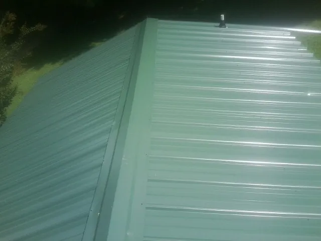 New green metal panels meeting at the ridge of a roof — Flat Roof Repair work by our crew in Ocean Isle Beach