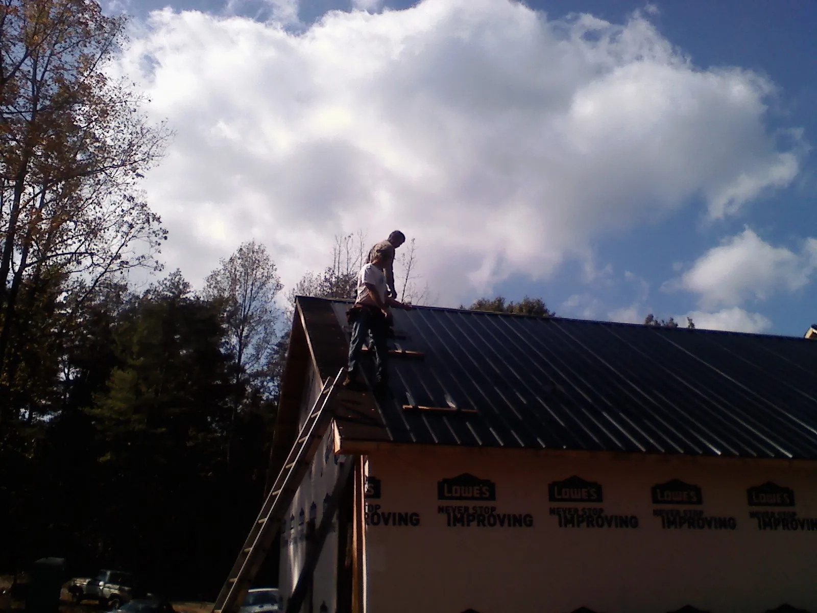 Roofer fastening dark metal panels high against a cloudy sky, from a Roof Inspection job in Ocean Isle Beach