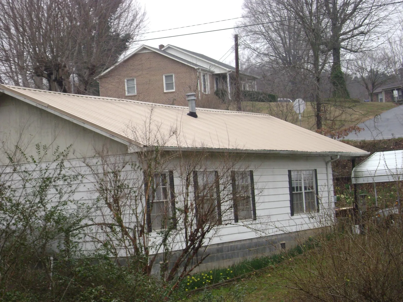 Tan metal roof on a white sided house set into a hillside — Commercial Roofing by Roofing Brothers in Ocean Isle Beach