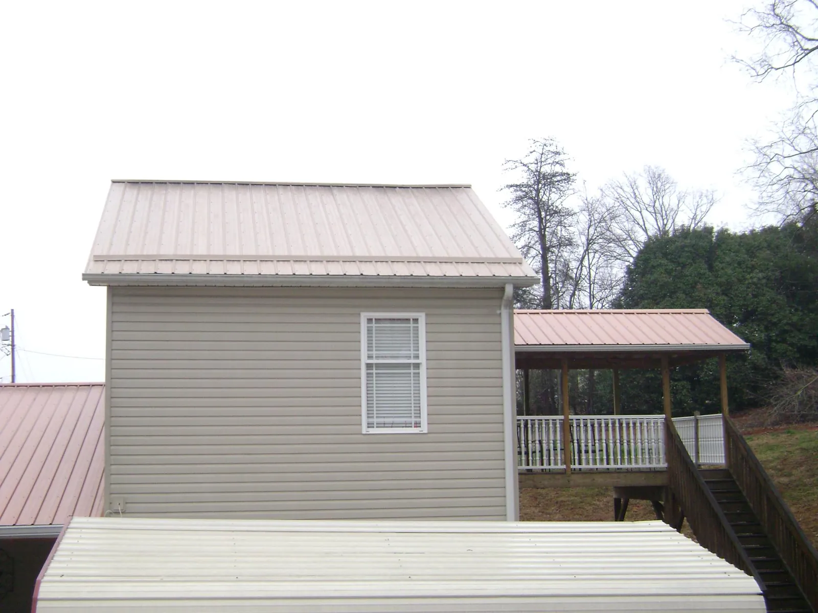 Tan metal roofs on a two story addition and attached porch, from a Roof Replacement job in Ocean Isle Beach