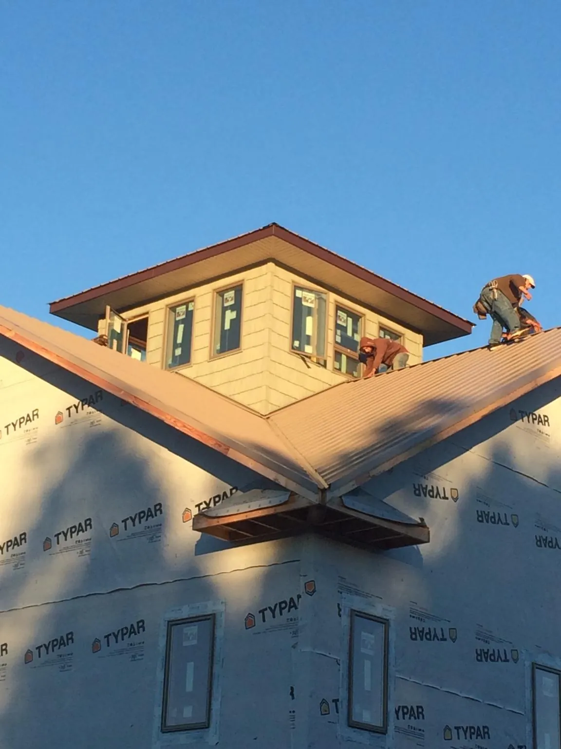 Roofers working around a rooftop cupola on a new metal roof at sunset — Roof Waterproofing in Ocean Isle Beach by Roofing Brothers
